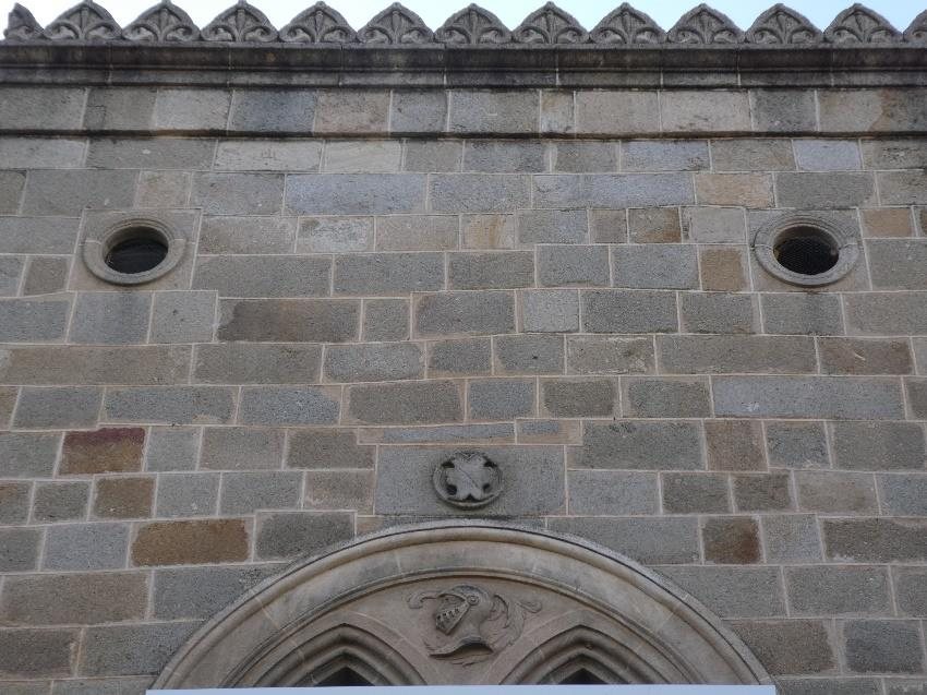 Cornisa dentada, pequeñas ventanas circulares y escudo en lo alto de la fachada